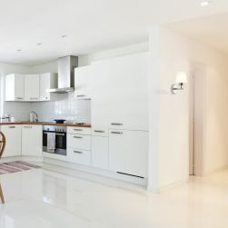kinkiet LEE CHROME 1xG9 w białym korytarzu z widokiem na białą kuchnię