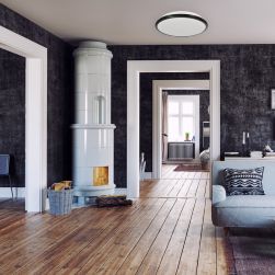 Przytulne wnętrze domu z drewnianą podłogą i ciemnymi ścianami, białym kominkiem, szarą kanapą i plafonem Terma Black