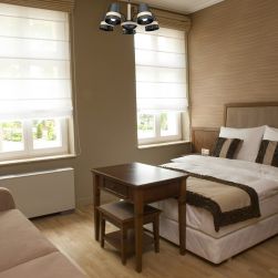 Mała sypialnia w drewnie z podwójnym łóżkiem, brązową kanapą, kwadratowym sekretarzykiem oraz czarnym żyrandolem w stylu skandynawskim Venezia black 5xE27 Milagro