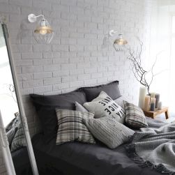 Ceglana sypialnia z szarym łóżkiem, białym lustrem i białymi kinkietami