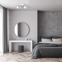 Sypialnia z szarymi ścianami, łóżkiem, białym stolikiem z pufą i okrągłym lustrem oraz z białą lampą sufitową Joker White