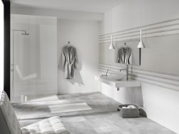 Łazienka z białymi ścianami i podłogą wyłożoną szarymi płytkami imitującymi beton Shark-S Natural z kabiną prysznicową, wiszącą półką z umywalką nablatową, lustrem, szlafrokiem i fotelem