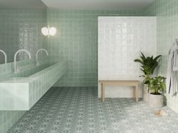 Zielona łazienka z jedną ścianką wyłożoną białymi cegiełkami kwadratowymi w połysku Nador White, z wiszącą półką z długą umywalką, dużym lustrem, ławą, kwiatami i szlafrokiem