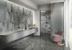 Nowoczesna, elegancka łazienka z fragmentem ściany wyłożonym płytą wielkoformatową imitującą metal Narciso Topazio, z kabiną prysznicową, wiszącą półką z dwiema umywalkami wpuszczanymi, dwoma okrągłymi lustrami i różowym fotelem