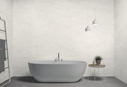 Łazienka z szarą podłogą i ścianami wyłożonymi białymi płytkami imitującymi kamień Nature White, z wanną wolnostojącą, okrągłym stoliczkiem, drabiną z ręcznikami i lampą wiszącą