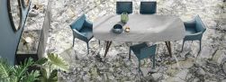 Jadalnia wyłożona płytkami imitującymi marmur Marmi Maxfine Ocean White, z szarym stołem, niebieskimi krzesłami i komodą