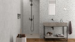 Szara łazienka z kabiną prysznicową, marmurową umywalką, prostokątnym podłużnym lustrem, białą lampą wiszącą, ręcznikami i płytkami drewnopodobnymi At.Rainier Nogal 20x120