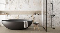 Elegancka łazienka ze ścianą wyłożoną płytkami imitującymi marmur Pisa Gold z czarną wanną owalną, kabiną prysznicową, taboretem i kosmetykami
