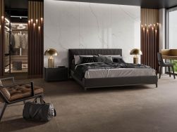Elegancka sypialnia ze ścianą wyłożoną płytkami imitującymi marmur Desert Natural z dużym łóżkiem, złotymi lampami, fotelem i garderobą