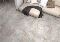 Zbliżenie na podłogę wyłożoną płytkami imitującymi beton z kolekcji Argile z beżową kanapą z poduszkami i ciemnym kocem