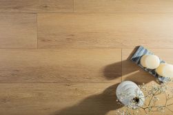 Widok z g&oacute;ry na podłogę z podłużnych paneli o odcieniu naturalnego, miodowego drewna dębowego. W prawym dolnym rogu stoją dekoracje: ceramiczny biały wazon z drobnymi kwiatami gips&oacute;wki oraz dwie jasne świece na marmurowej podstawce.