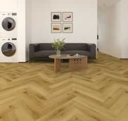 Wizualizacja nowoczesnego salonu z miodową podłogą ułożoną w jodełkę klasyczną. W centrum stoi ciemnoszara sofa, przed nią designerski, drewniany stolik kawowy. Po lewej stronie wbudowano w białą ścianę pralkę i suszarkę bębnową.
