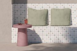 Taras z betonową ławą wyłożoną patchworkowymi płytkami Patterns Pink Geometric z dwoma zielonymi poduszkami i okrągłym różowym stolikiem