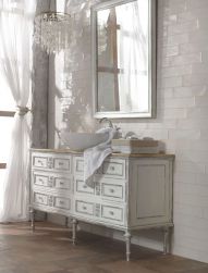 Romantyczna łazienka ze starą, białą szafką z szufladami i owalną umywalką nablatową, lustrem w białej ramie, żyrandolem, oknem z białą, zwiewną zasłoną i jasnymi cegiełkami na ścianie z kolekcji Poitiers
