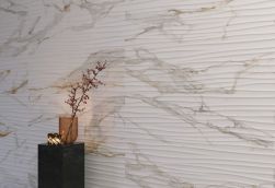 Ściana wyłożona białymi płytkami imitującymi marmur ze strukturalną powierzchnią Praline Gold z czarnym, marmurowym stolikiem ze świeczkami i wazonem z gałązką