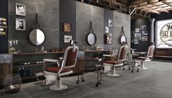 Ciemny salon fryzjerski ze ścianą wyłożoną płytkami imitującymi kamień Groove Mistique Black, z trzema stanowiskami, krzesłami, okrągłymi lustrami, kosmetykami i zdjęciami na ścianach