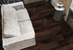 Widok z góry na podłogę wyłożoną ciemnymi płytkami imitującymi drewno Provoak Nero Bruciato, z jasną kanapą
