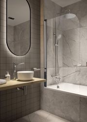Łazienka wyłożona płytkami imitującymi kamień z wanną z parawanem prysznicowym oraz wiszącym blatem z okragłą umywalką Jasmin i owalnym lustrem