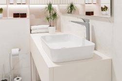Jasna łazienka z białą szafką z białą umywalką nablatową Deante Hiacynt New ze stojącą baterią w chromie, lustrem, rośliną w doniczce oraz akcesoriami