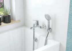 Fragment jasnej łazienki z białą wanną i baterią wannową ścienną Deante Chaber ze słuchawką prysznicową