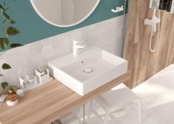 Przytulna łazienka z drewnianym blatem z umywalką nablatową z białym korkiem klik-klak i białą baterią stojącą, okrągłym lustrem i kabiną prysznicową