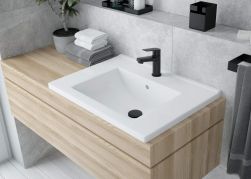Jasna, drewniana szafka w łazience z białą umywalką wpuszczaną w blat Deante Floks z czarnym korkiem i baterią stojącą oraz ręcznikami i akcesoriami