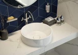 Blat łazienkowy imitujący marmur, na blacie biała umywalka, płytki ścienne w niebieskim kolorze, na blacie akcesoria łazienkowe, na ścianie Deante Round Dozownik mydła - ścienny chrom ADR_0421