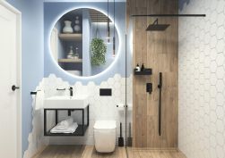 jasna łazienka z drewnianymi płytkami i niebieską ścianą za podświetlanym lustrem, białą armatura, czarne baterie, czarna wisząca mydelniczka Mokko na ścianie z lewej obok drzwi, białe ręczniki pod umywalką