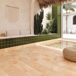Pomieszczenie z basenem z podłogą wyłożoną beżowymi, rustykalnymi cegiełkami Roots L Sand z pufą, jasnymi poduszkami, ozdobą na ścianie i roślinami