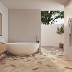 Łazienka z podłogą wyłożoną beżowymi, rustykalnymi cegiełkami Roots M Sand z białą wanną wolnostojącą, wiszącą szafką z umywalką nablatową, lustrem i szlafrokiem na ścianie