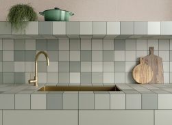 Ściana i blat w kuchni wyłożone zielonymi płytakmi bazowymi Rubik Sage ze zlewem, złotą baterią i naczyniami