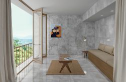 Pokój z balkonem wyłożony szarymi płytkami imitującymi beton Shark-S Lappato z beżową kanapą, okrągłym i prostokątnym stolikiem, dywanem, lampą stojącą i obrazem na ścianie