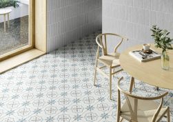 Podłoga w jadalni wyłożona patchworkowymi płytkami z kwiatowym motywem Sirocco Blue Cross z okrągłym stołem, dwoma krzesłami i oknem