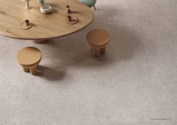 Widok z góry na podłogę wyłożoną płytkami imitującymi beton z kolekcji Sixty z drewnianym, okrągłym stołem oraz taboretami