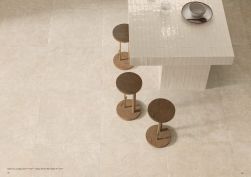 Widok z góry na podłogę wyłożoną beżowymi płytkami imitującymi beton z kolekcji Sixty, ze stołem zabudowanym cegiełkami w połysku i trzema taboretami drewnianymi