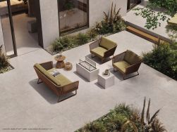 Otwarty taras wyłożony płytkami imitującymi beton z kolekcji Sixty z kanapą oraz dwoma fotelami, stolikami i dużą ilością zieleni