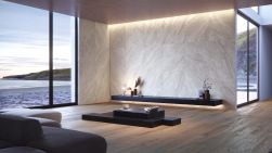 Przestronny salon ze ścianą wyłożoną wielkoformatowymi płytkami imitującymi kamień Strond Cloud SP i brązową, drewnopodobną podłogą z długą, marmurową, czarną półką i stołem oraz kanapą