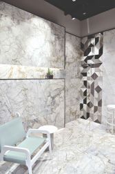 Łazienka wyłożona jasnymi płytkami imitującymi marmur Supreme White SP z kabiną prysznicową walk-in, białym okrągłym stolikiem oraz szerokim krzesłem