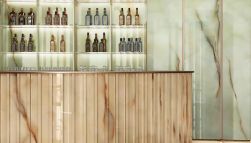 Bar ze ścianą wyłożoną zielonymi płytkami imitującymi kamień onyks z kolekcji Tele di Marmo Pure Onyx z ladą, półkami i alkoholem
