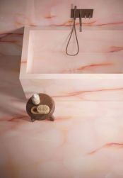 Podłoga, ściana oraz wanna w łazience wyłożone różowymi płytkami imitującymi kamień onyks z kolekcji Tele di Marmor Pure Onyx