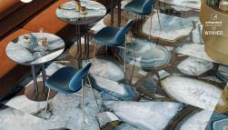 Podłoga w restauracji wyłożona niebieskimi płytkami imitującymi kamień z kolekcji Tele di Marmo Precious z okragłymi stolikami, brązową kanapą i niebieskimi krzesłami