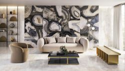 Elegancki salon wyłożony płytkami imitującymi kamień z kolekcji Tele di Marmo Precious z kanapą, fotelem, stolikiem i regałem z ozdobami
