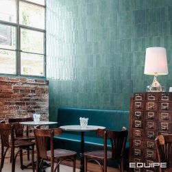 Restauracja z ceglaną ścianą pod oknem, niebieską kanapą, okrągłymi stolikami z krzesłami, szafką vintage z lampką stojącą i błękitnymi cegiełkami ściennymi z kolekcji Tribeca
