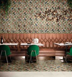 Restauracja, stoliki z zielonymi krzesłami, pod ścianą brązowa kanapa, ściana i podłoga wyłożone Tropical Tucanas Natural 30,5x30,5 płytki z motywem tropikalnym
