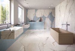 Jasna łazienka z jedną ścianą wyłożoną płytkami imitującymi marmur Unique Marble Ambra Paonazzetto, z drewnianą wanną, dwoma wiszącymi umywalkami marmurowymi i dwoma oknami