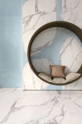 Pomieszczenie wyłożone jasnymi płytkami imitującymi marmur z kolekcji Unique Marble Marmo Calacatta Regale, z okrągłym siedziskiem wiszącym z poduszkami