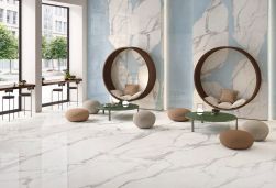 Nowoczesna restauracja wyłożona płytkami imitującymi marmur z kolekcji Unique Marble Calacatta Regale, z okrągłymi stolikami, pufami, okrągłymi siedziskami, stolikami pod oknami i krzesłami