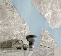Widok na ścianę wyłożoną płytkami imitującymi kamień z kolekcji Unique Marble Ambra Moon Grey, z szafką i wazonami