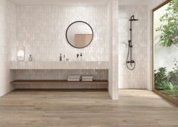 Łazienka ze ścianą wyłożoną białymi cegiełkami i podłogą wyłożoną brązowymi płytkami drewnopodobnymi Verbier Taupe z prysznicem, wiszącą półką z umywalką i okrągłym lustrem