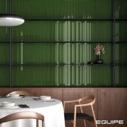Ściana w restauracji wyłożona zielonymi cegiełkami dekoracyjnymi w połysku Vitral Axis Forest, z okrągłym stołem z obrusem i zastawą oraz krzesłami